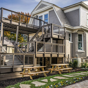 A two story light grey house with a combined dark wood two story deck and balcony.