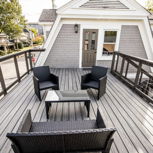 Modern grey home deck with black chairs, couch, and coffee table door to go into the home in the back