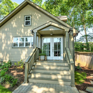 A tan house with a small covered porch surrounded by neat landscaping.