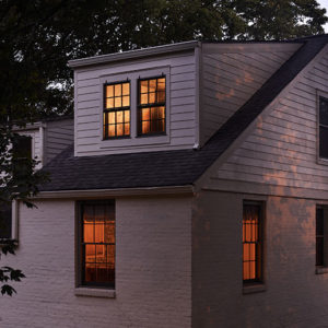 An outdoor view of a two story house at dusk with a new top floor addition.