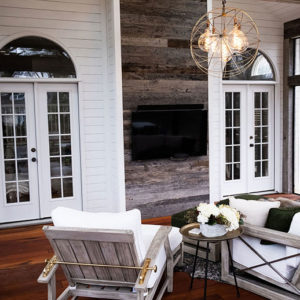 The inside view of an enclosed deck with rustic wood accents. Their are two white windowed doors leading into the house.