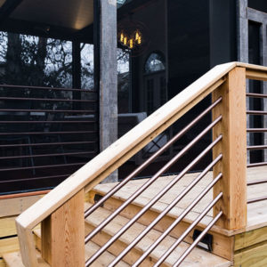 An upclose view of a natural wood and metal railing on the side of a house with floor length windows.