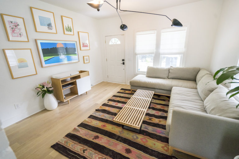 A white wall living room with a grey couch and wood coffee table with serval colorful pictures on the wall in front of it