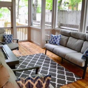 Screened in porch with hardwood floors and grey furniture with blue pillows