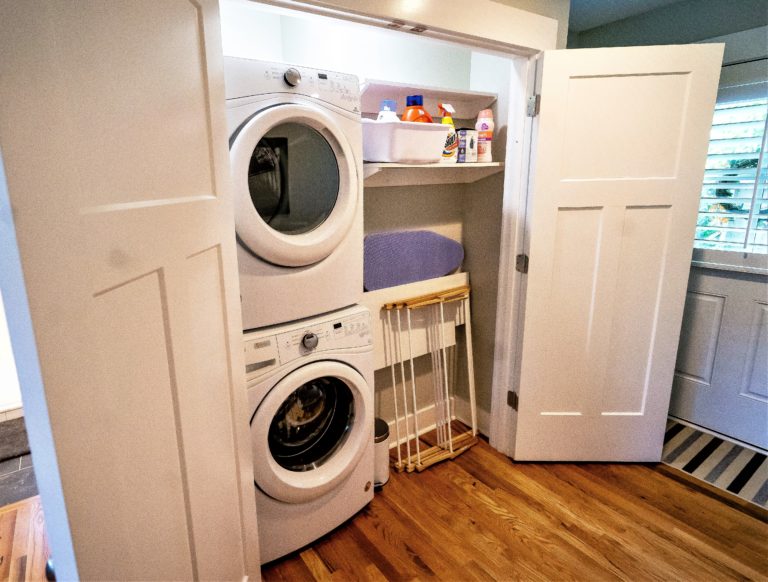 A closet with a stacked washer and dryer, a folded hanging rack, and a shelf with laundry products