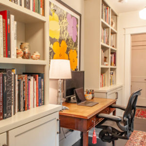 Two bookshelves filled with books, a desk sitting in between the bookshelves with a large foral painting overhead