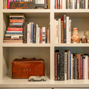 White bookshelf with assortment of books, a small car, and suitcase