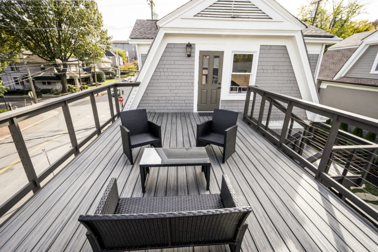 Modern grey home deck with black chairs, couch, and coffee table door to go into the home in the back