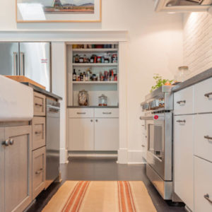 A low picture of cabinets and kitchen oven with a pantry in the background and an orange rug on the hardwood floors