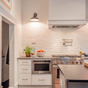 Kitchen with white backsplash, stainless steal oven, microwave, grey countertops, with light on the wall above