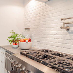 A stainless steel gas stove with white backsplash, and two bowls of apples on the counter