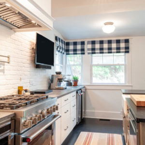 White kitchen with dark blue curtains above two windows, a tv above the counter, a stainless steel oven, and white cabinets