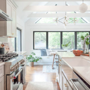 White kitchen with stainless steel appliances, kitchen island, and four large windows with natural lighting