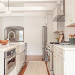 A low picture of cabinets and kitchen oven with a pantry in the background and an orange rug on the hardwood floors