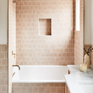 A cream tile shower with a cut out shelf and a sink and white granite countertops