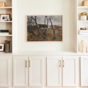 Picture of trees and a home centered on a white wall with bookshelves on both sides and white cabinets underneath