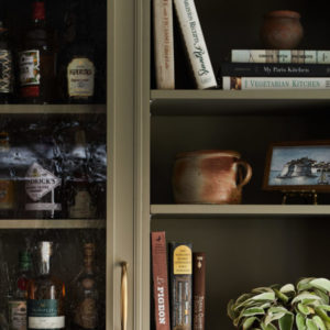 A bookshelf with a piece of pottery, books, a plan and picture, and liquor bottles