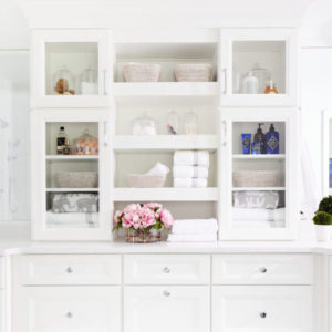 White organizer with towels and vases on shelves and drawers underneath