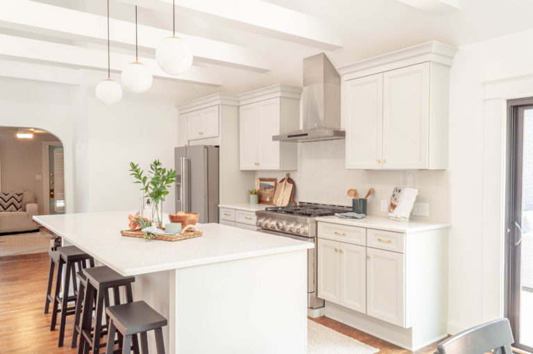 White kitchen with stainless steel appliances and large island with chairs underneath the counter