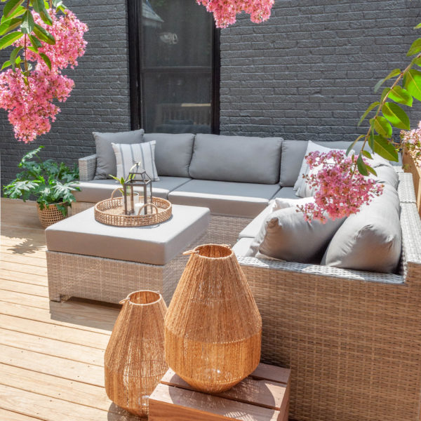 Patio with light gray couch and ottoman and pink flowers on the sides of the frame