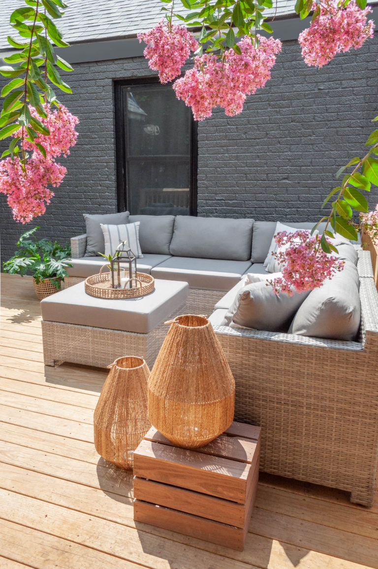 Patio with light gray couch and ottoman and pink flowers on the sides of the frame