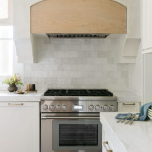 A stainless steel oven with a wood accent range hood and gray- white backsplash.