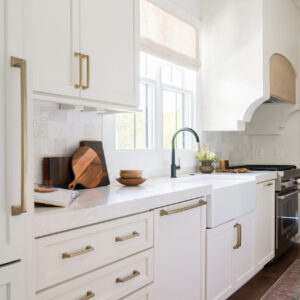 A beautiful modern kitchen remodel with white cabinets, marble countertops, and gold handles.