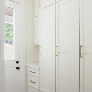 A naturally lit white kitchen pantry addition next to a windowed door leading outside.