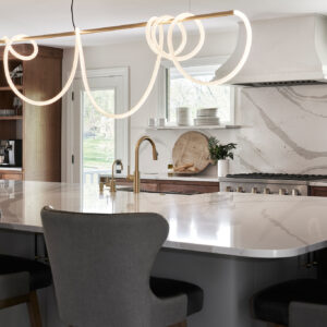 A close up shot of a kitchen island with a marble top with a custom Luke Lamp company light over the island.