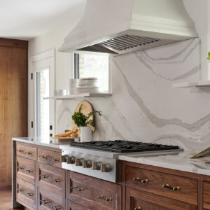 A custom kitchen vent hood over a cooktop. Below the vent are custom wood cabinets with a marble countertop.