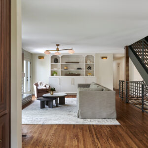 A side view of a new living room remodel. A gray couch sits in the middle of the room with a gray brick fireplace in front.