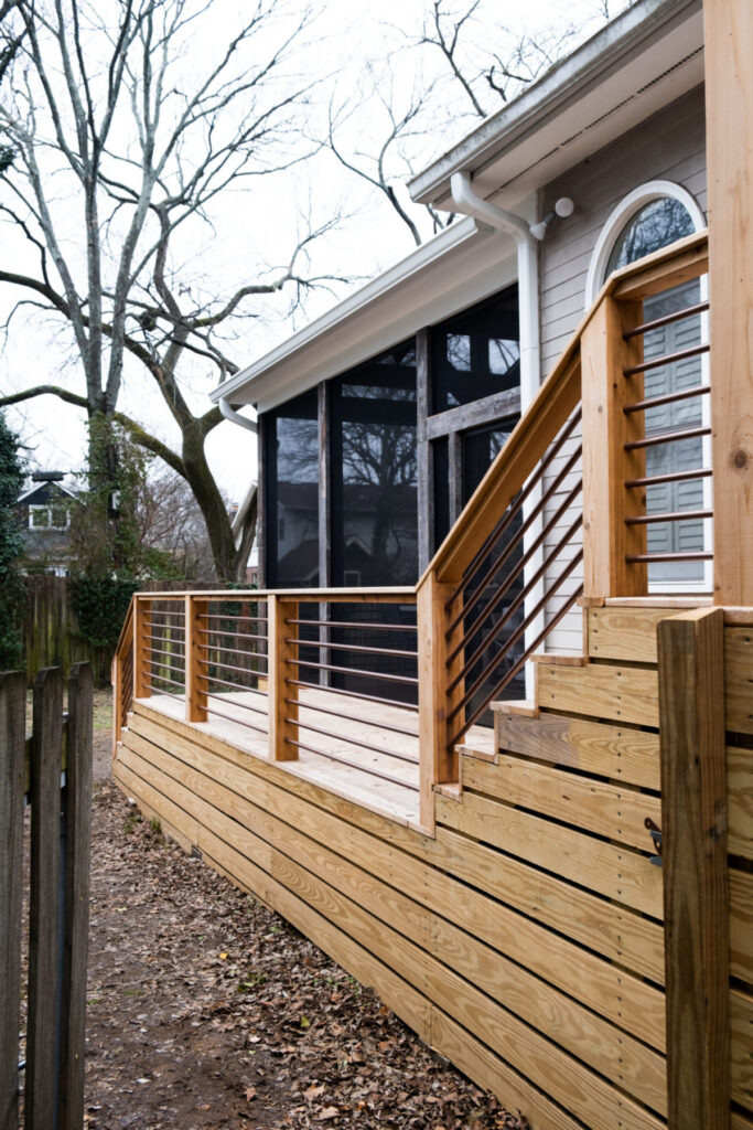 Elevated wooden deck with modern cable railing attached to the back of a house.