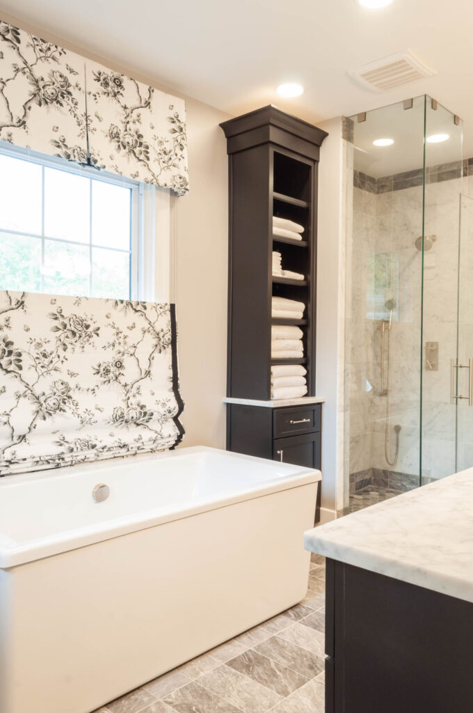 A sleek bathroom with a white freestanding tub, marble countertops, a glass-enclosed shower, and built-in storage cabinets.