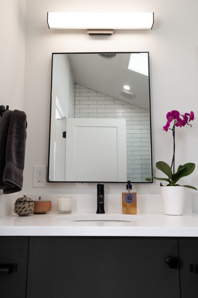 Modern bathroom vanity with a square mirror, sleek lighting, and a countertop featuring a purple orchid and essentials.