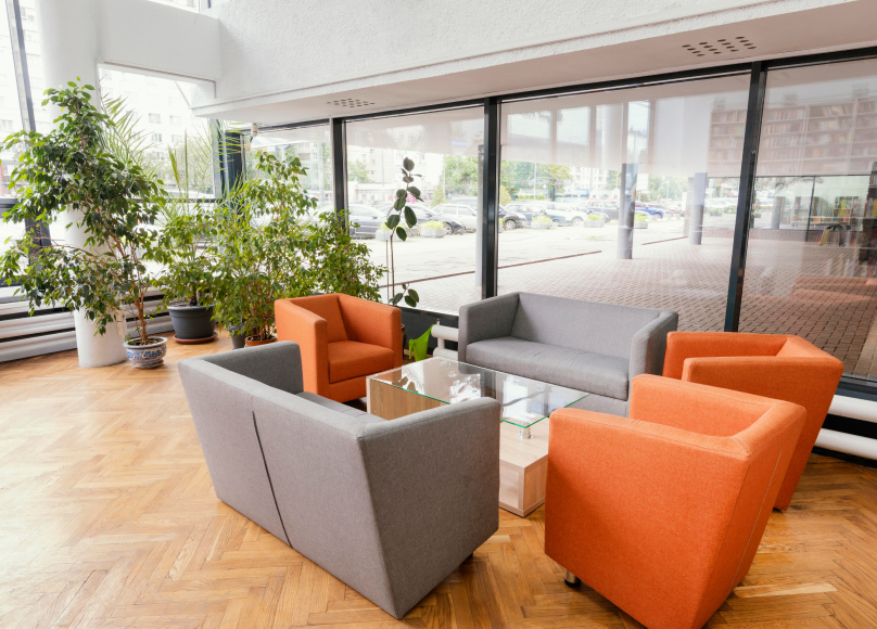 Business lounge area with orange and gray seating surrounded by large windows.
