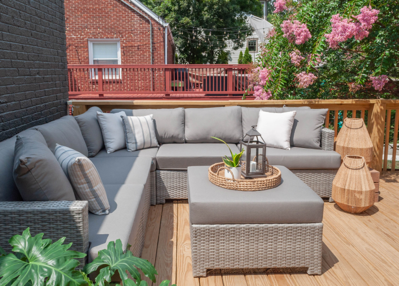 An elegant deck featuring a modern wicker sectional, neutral cushions, and accent decor under vibrant greenery.