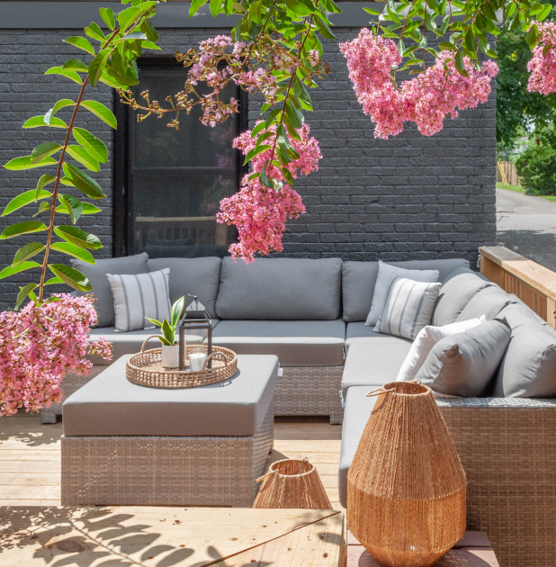Cozy outdoor patio with gray sectional seating and pink flowers.