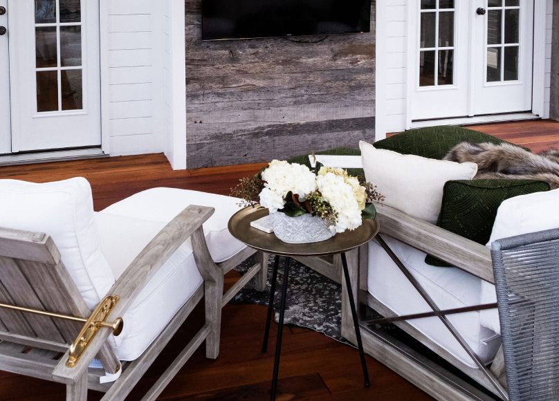 An inviting outdoor lounge with plush white seating, rustic wooden accents, and floral arrangements under a sheltered patio.