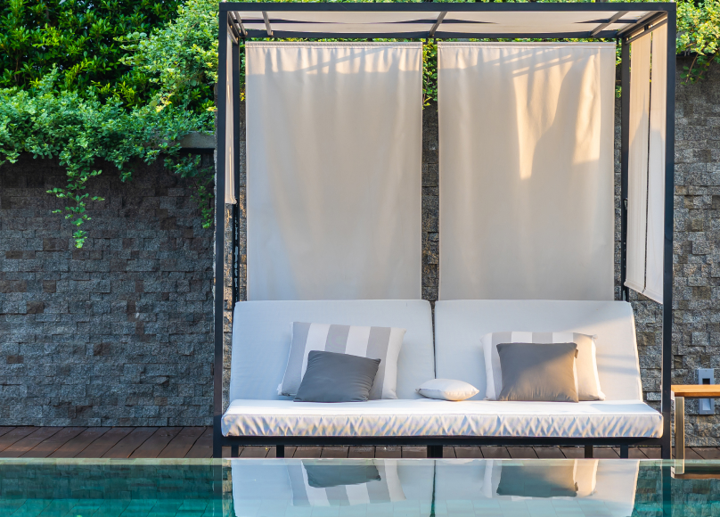 A chic cabana setup with white canopy curtains and cushioned seating, reflecting beautifully off the pool water.