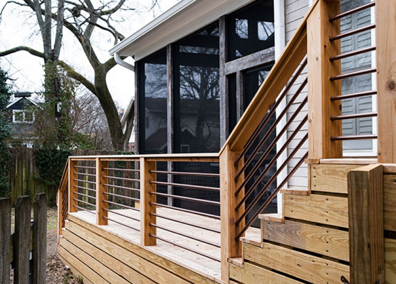 Wooden deck with elegant railing surrounding a screened porch addition.
