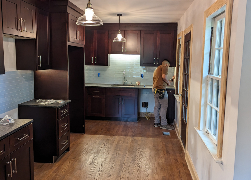 Handyman working on kitchen cabinetry with dark wood finish.