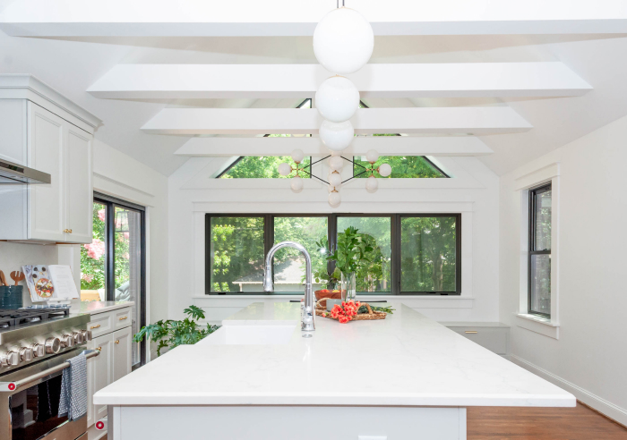 Bright kitchen with a large central island, vaulted ceiling beams, and ample natural light from expansive windows.