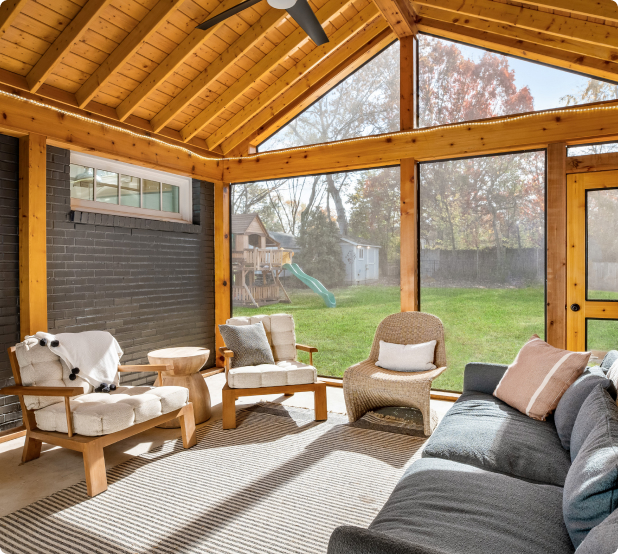A beautifully designed screened-in porch with wooden beams, cozy seating, and a scenic backyard view.