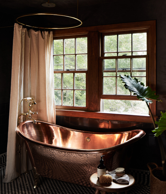 Luxury bathroom with a copper freestanding tub, large windows, and dark, elegant decor.