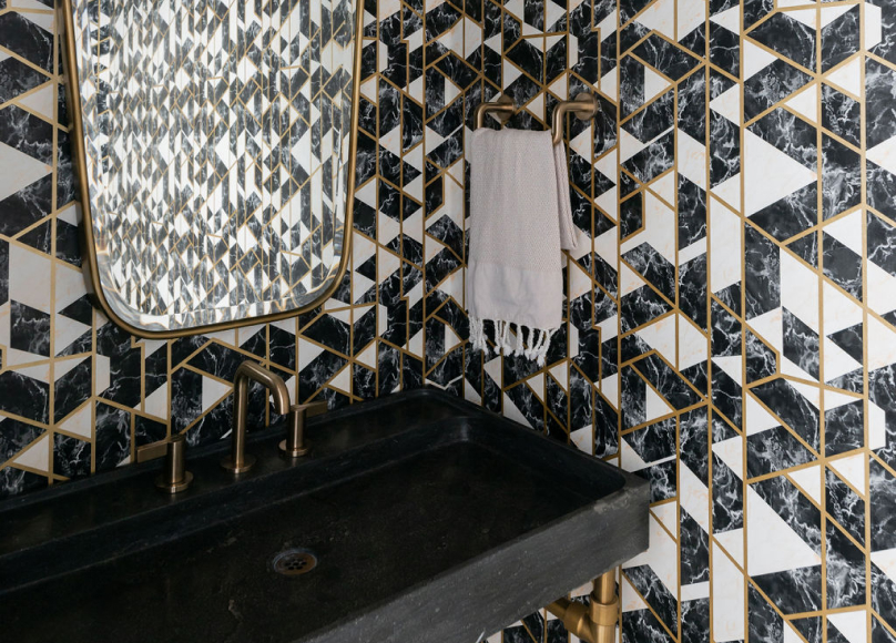 Bold bathroom design with geometric wall tiles, a black sink, and gold accents.