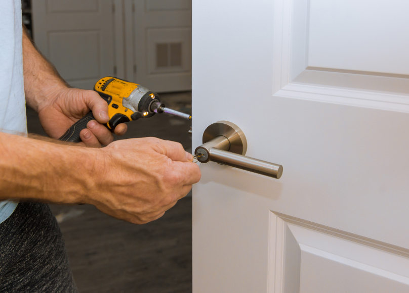 Worker installing a new door handle with a power drill.
