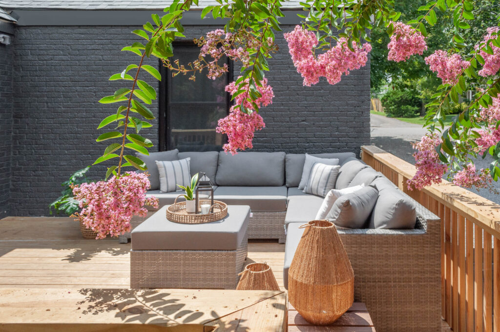 Cozy outdoor patio with gray sectional seating and pink flowers.